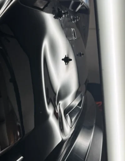 Dent on a black car's rear panel under a PDR reflection board