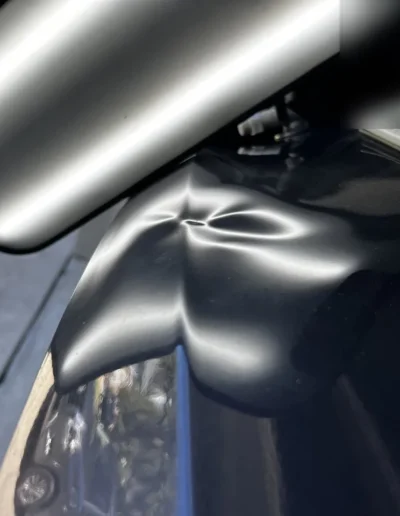 Dent on a black car's trunk lid before paintless dent repair