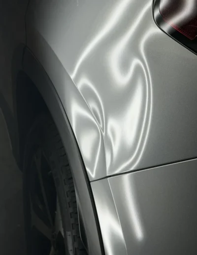 Dent above the rear wheel arch of a silver SUV before paintless dent repair